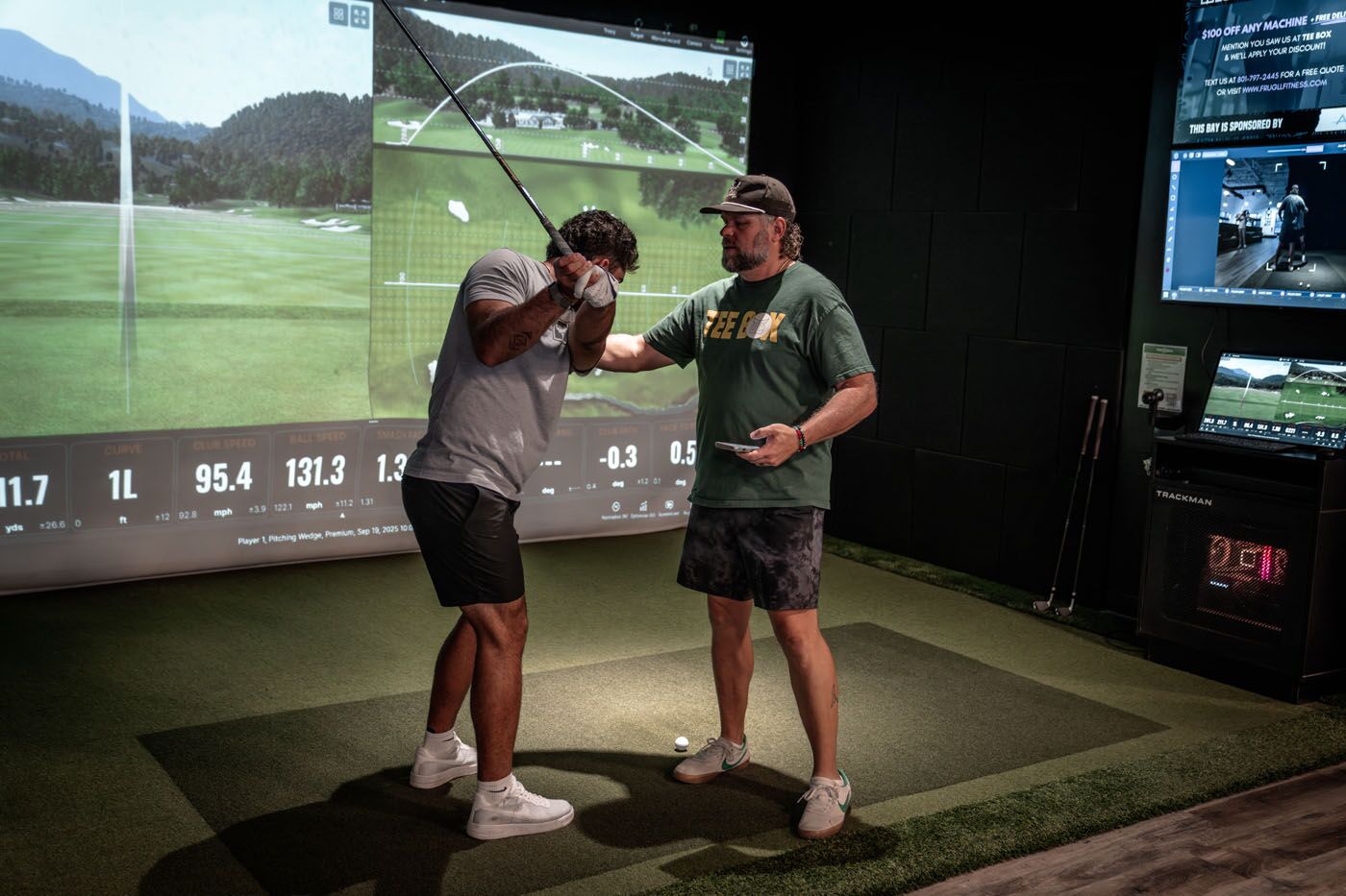A Tee Box coach helping a young man improve his swing while using an indoor driving range in Scottsdale, AZ.