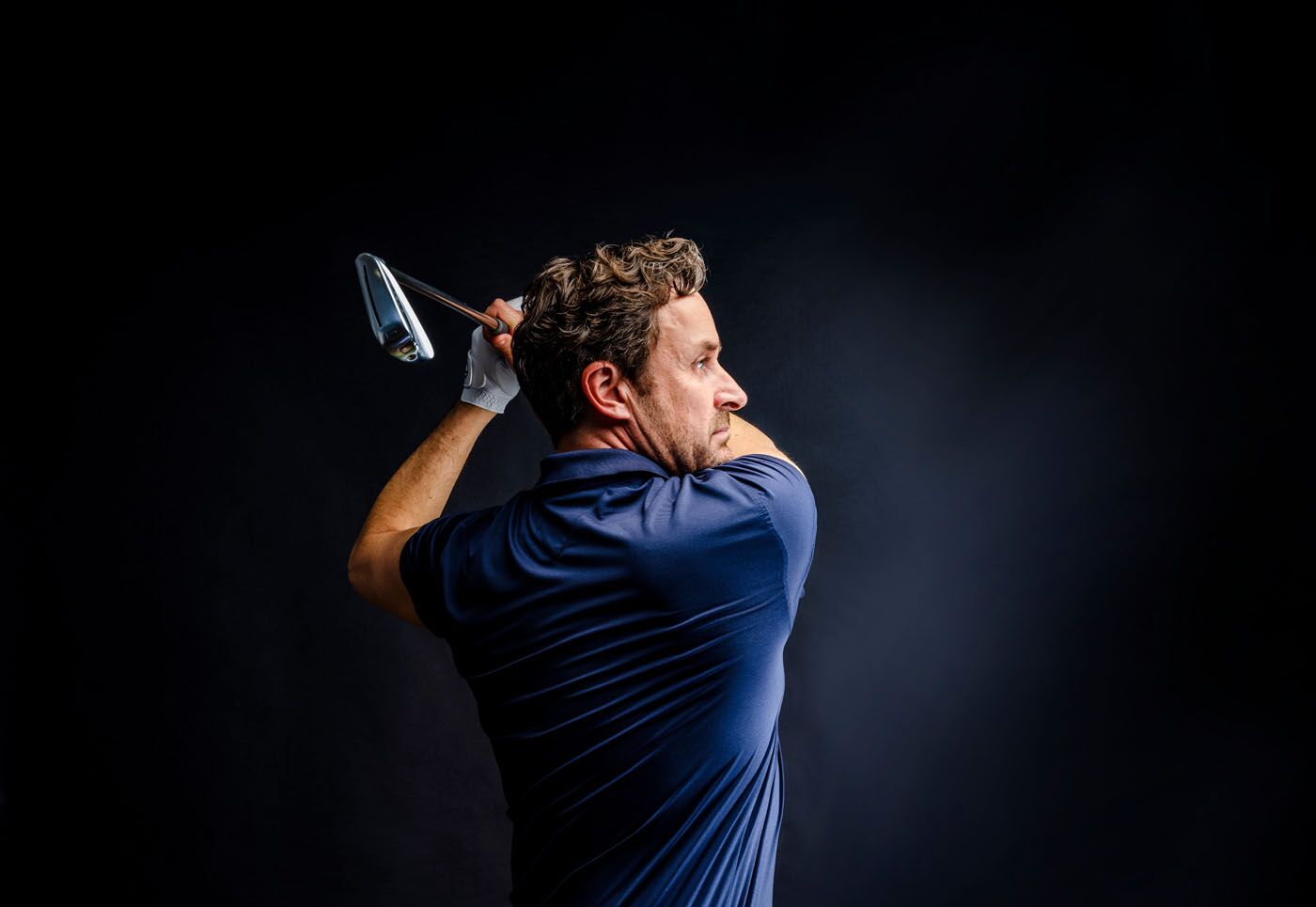 The profile of a man who is swinging his club in a Tee Box golf course in Scottsdale, AZ.