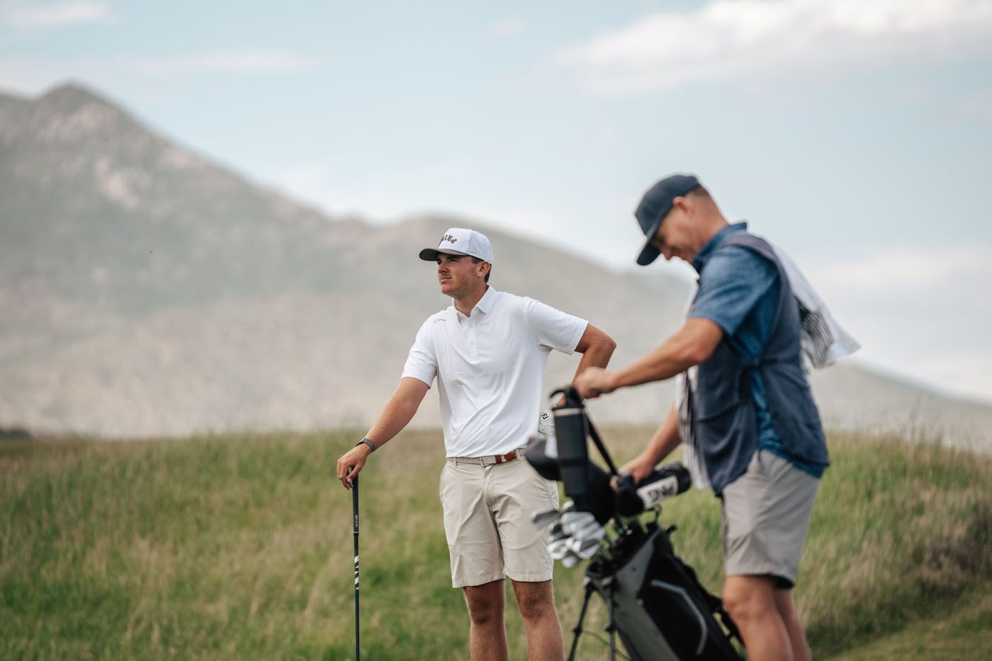 Two men in golf attire standing on and looking out over a golf course.